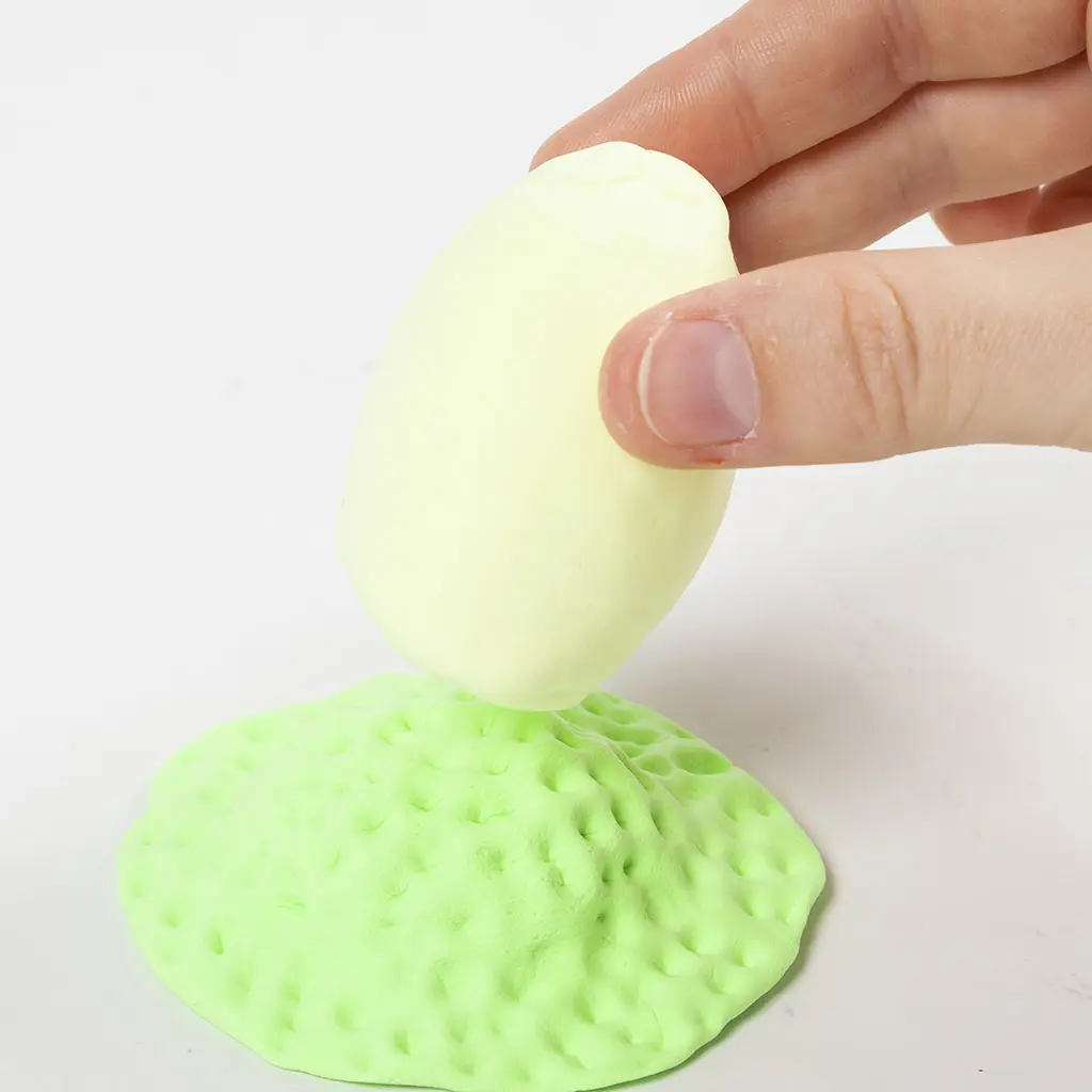Het verticaal plaatsen van het bedekte gele ei op het midden van de getextureerde groene kleibasis.