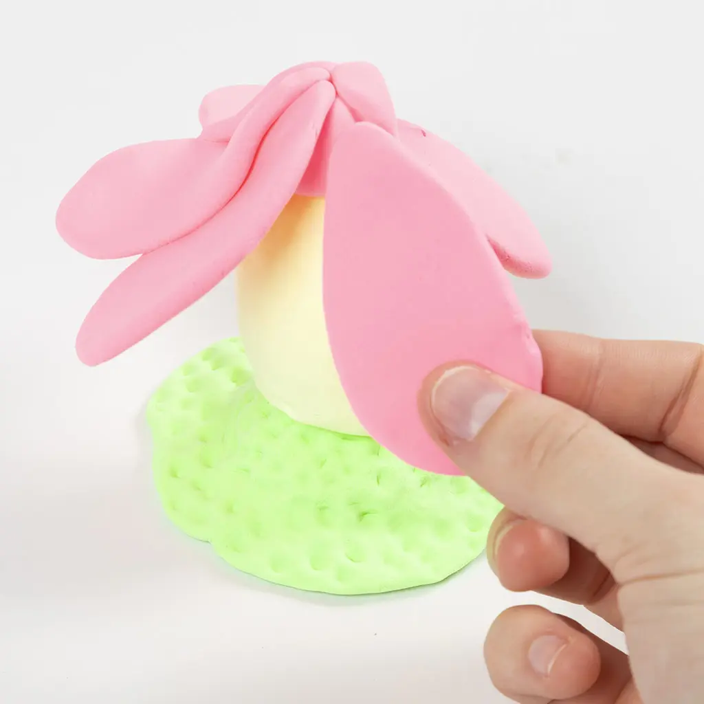 Een hand bevestigt roze kleibladeren rondom de top van het gele ei om een dak in de vorm van een bloem te bouwen.