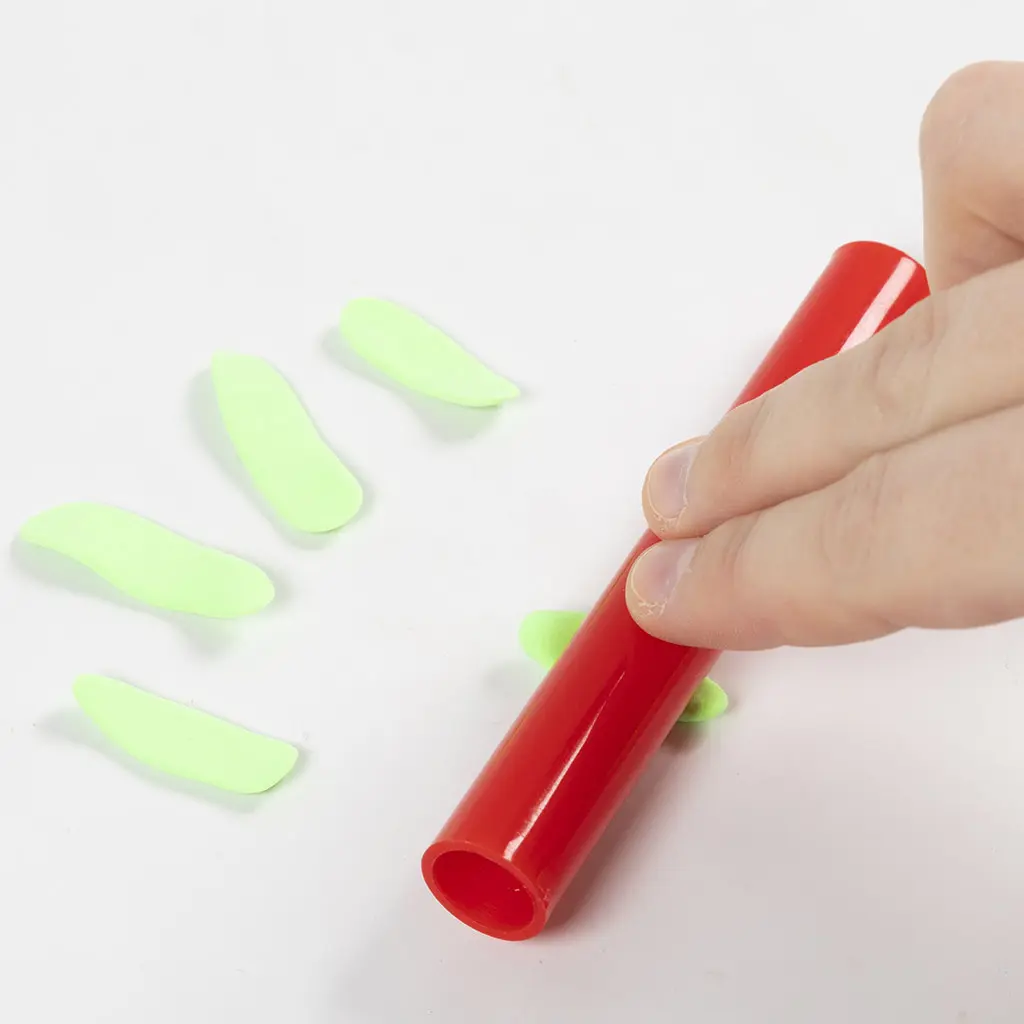 Een hand rolt kleine stukjes lichtgroene klei plat met de rode roller om het kelkje van het bloemendak te maken.