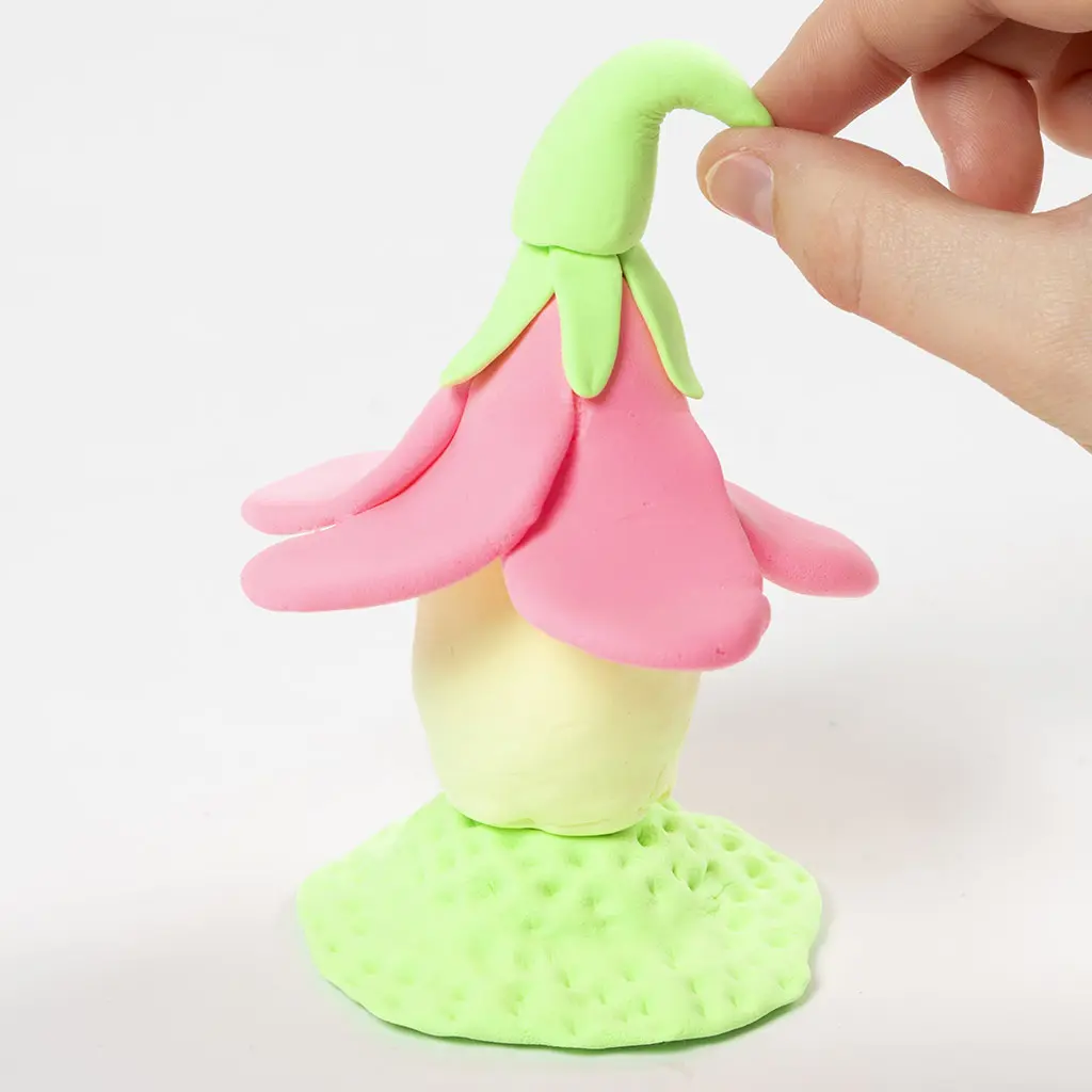 Een hand vormt een lichtgroen kleisteeltje op het dak tot een sierlijk gebogen piek.g