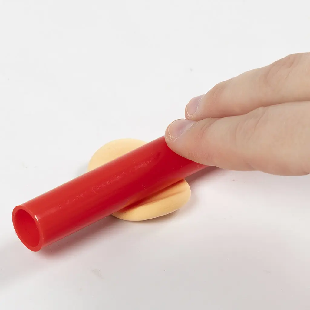 Het platrollen van een oranje/zalmkleurig stukje klei met de rode roller om een deurtje te maken.