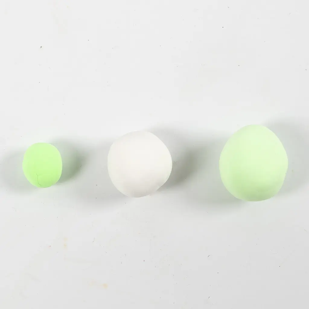 Drie op een rij gelegde kleibolletjes in lichtgroen, wit en een grotere lichtgroene bol op een witte achtergrond.