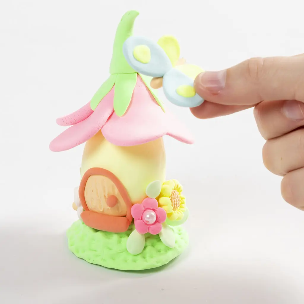 Een hand plaatst een gemodelleerde kleilibelle op de gebogen groene piek van het bloemendak.