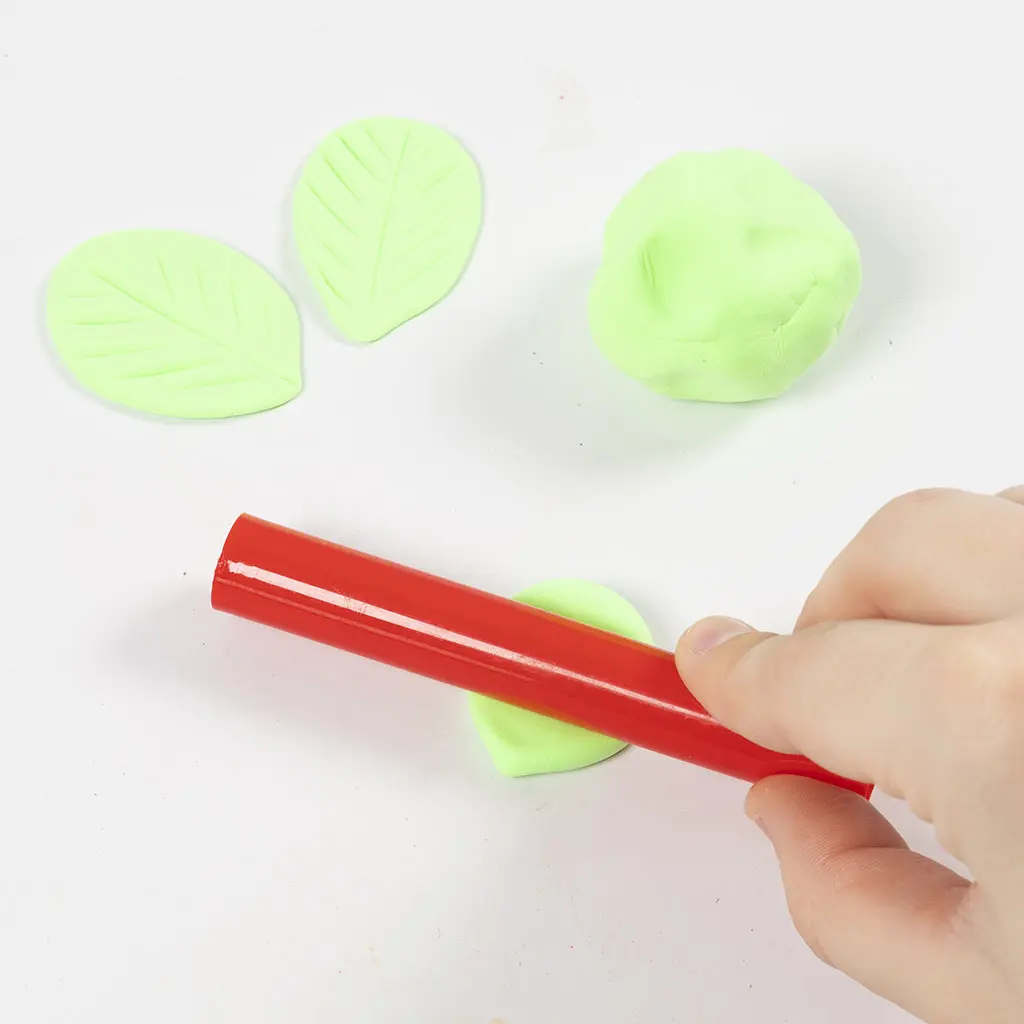 Een hand rolt de lichtgroene kleidruppel plat met een rode kunststof roller om een groter blad voor het dak te maken.