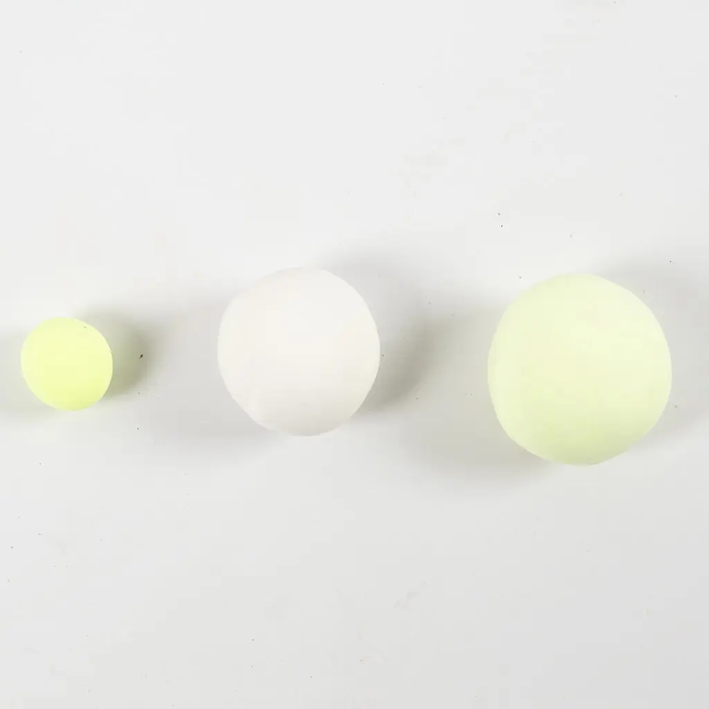 Drie op een rij gelegde kleibolletjes in fel geelgroen, wit en heel lichtgeel op een witte achtergrond.
