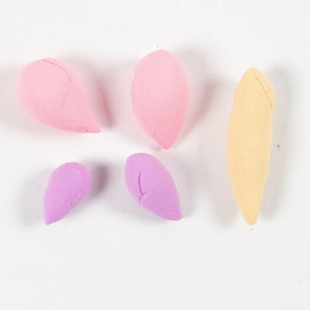 Klaargelegde onderdelen voor de vlinder: twee grote roze kleidruppels, twee kleine paarse kleidruppels en een geel ovaal lijfje op een witte ondergrond.
