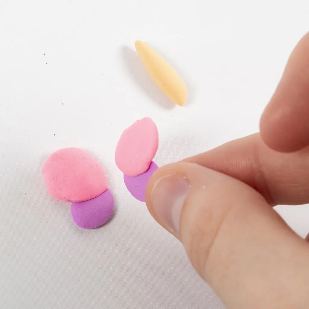 Een vinger drukt de roze en paarse kleidruppels plat en aan elkaar vast om de vlindervleugels te maken.