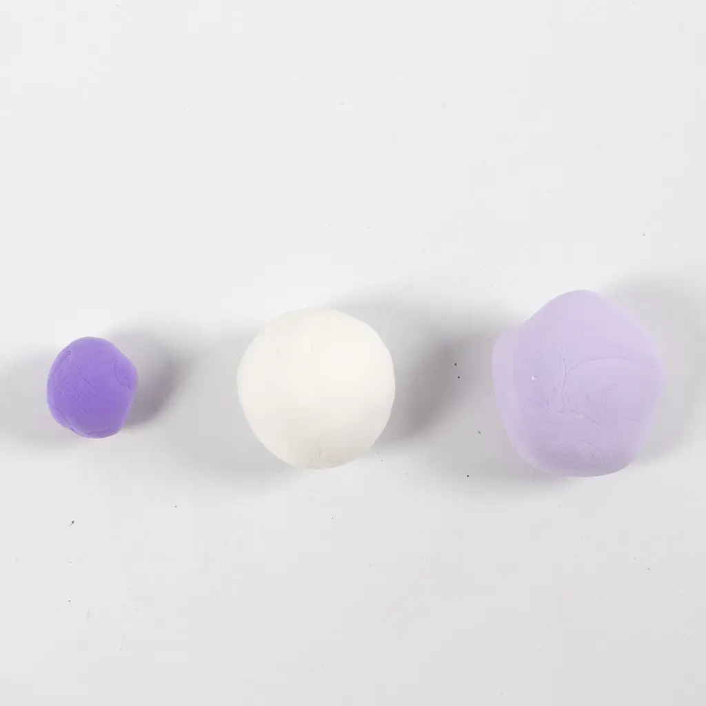 Drie op een rij gelegde kleibolletjes in felpaars, wit en lila op een witte achtergrond.