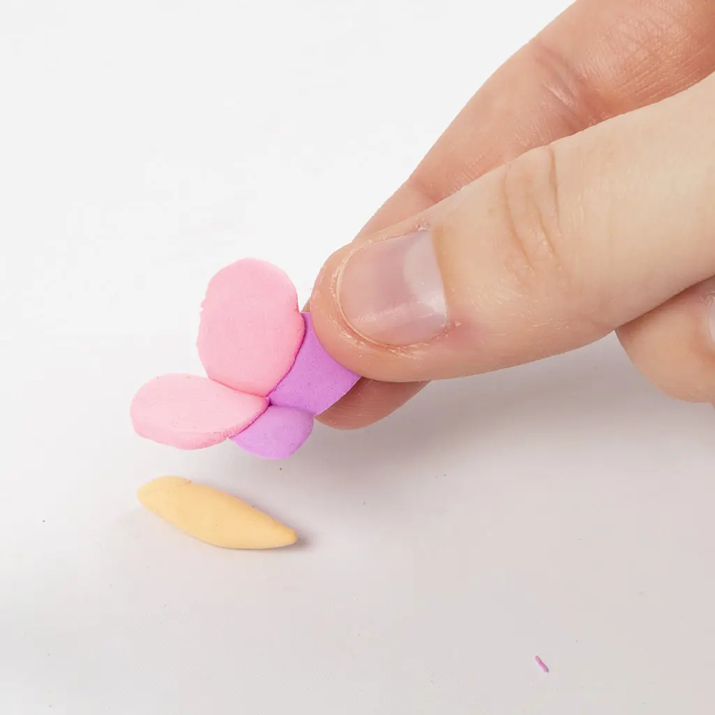 Een hand houdt de samengevoegde roze en paarse vlindervleugels omhoog, klaar om aan het gele vlinderlijfje te bevestigen.