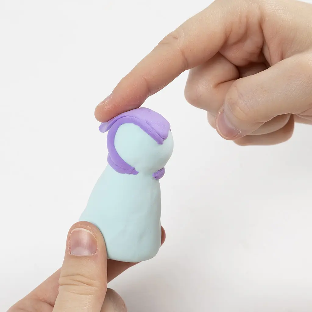 Een vinger strijkt de paarse klei aan de bovenkant glad om het hoofdgedeelte van het vlinderfiguurtje te vormen.