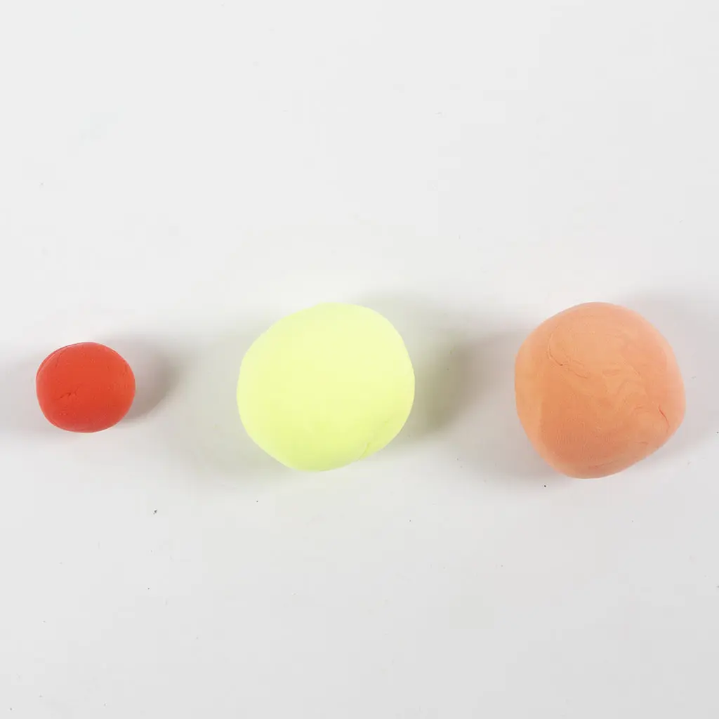 Drie op een rij gelegde kleibolletjes in rood, geel en een grotere oranje/huidskleurige bol op een witte achtergrond.
