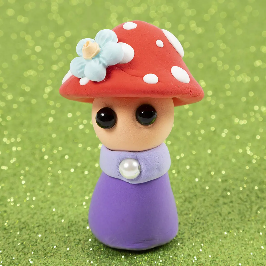 Een schattig boetseerfiguurtje van een paddenstoeltje met een paarse jurk, parel kraag, gezichtje met zwarte kraaloogjes en een rode hoed met witte stippen en een blauw bloemetje.